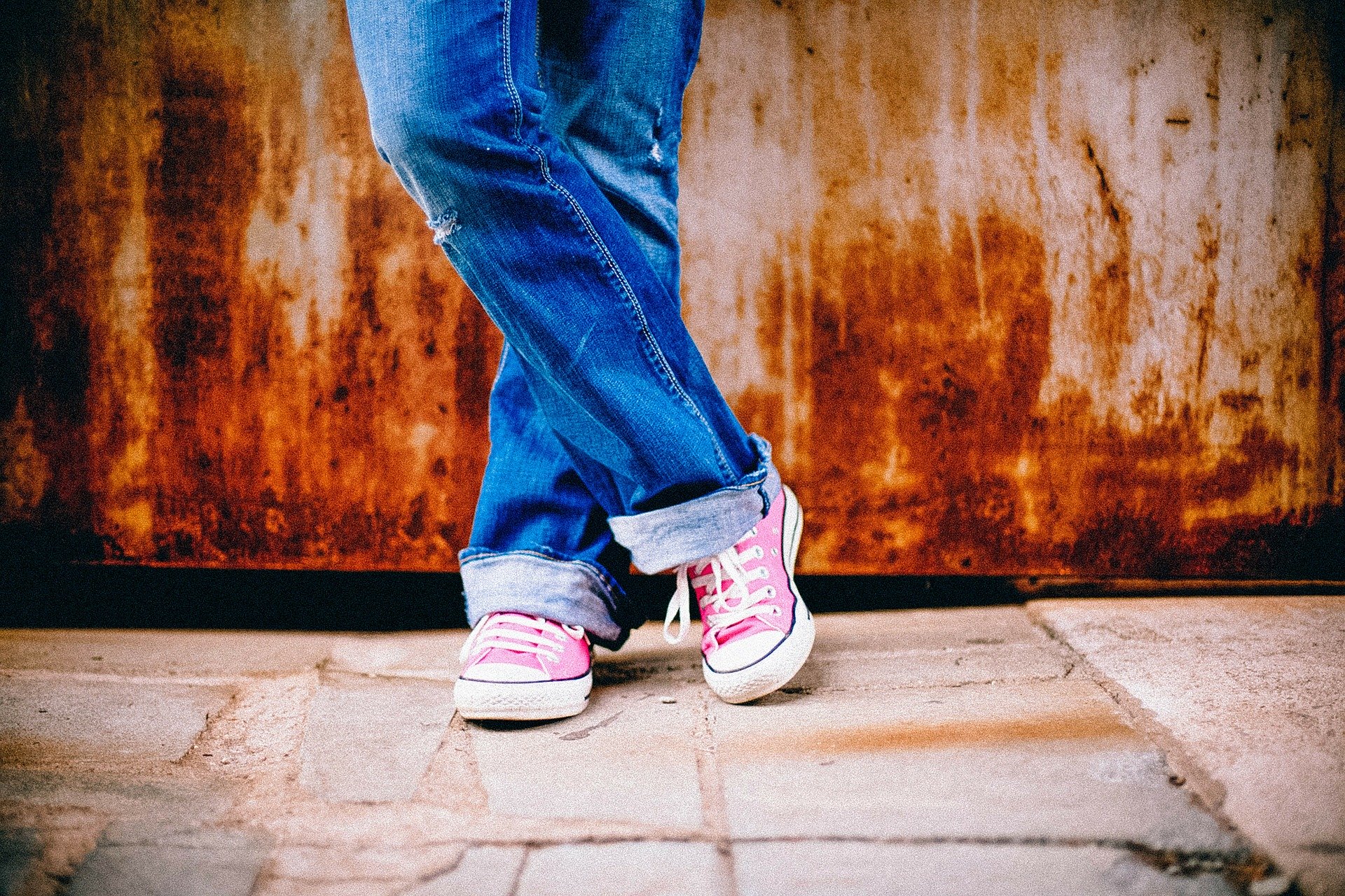 a person from the knees down, wearing blue jeans and pink sneakers