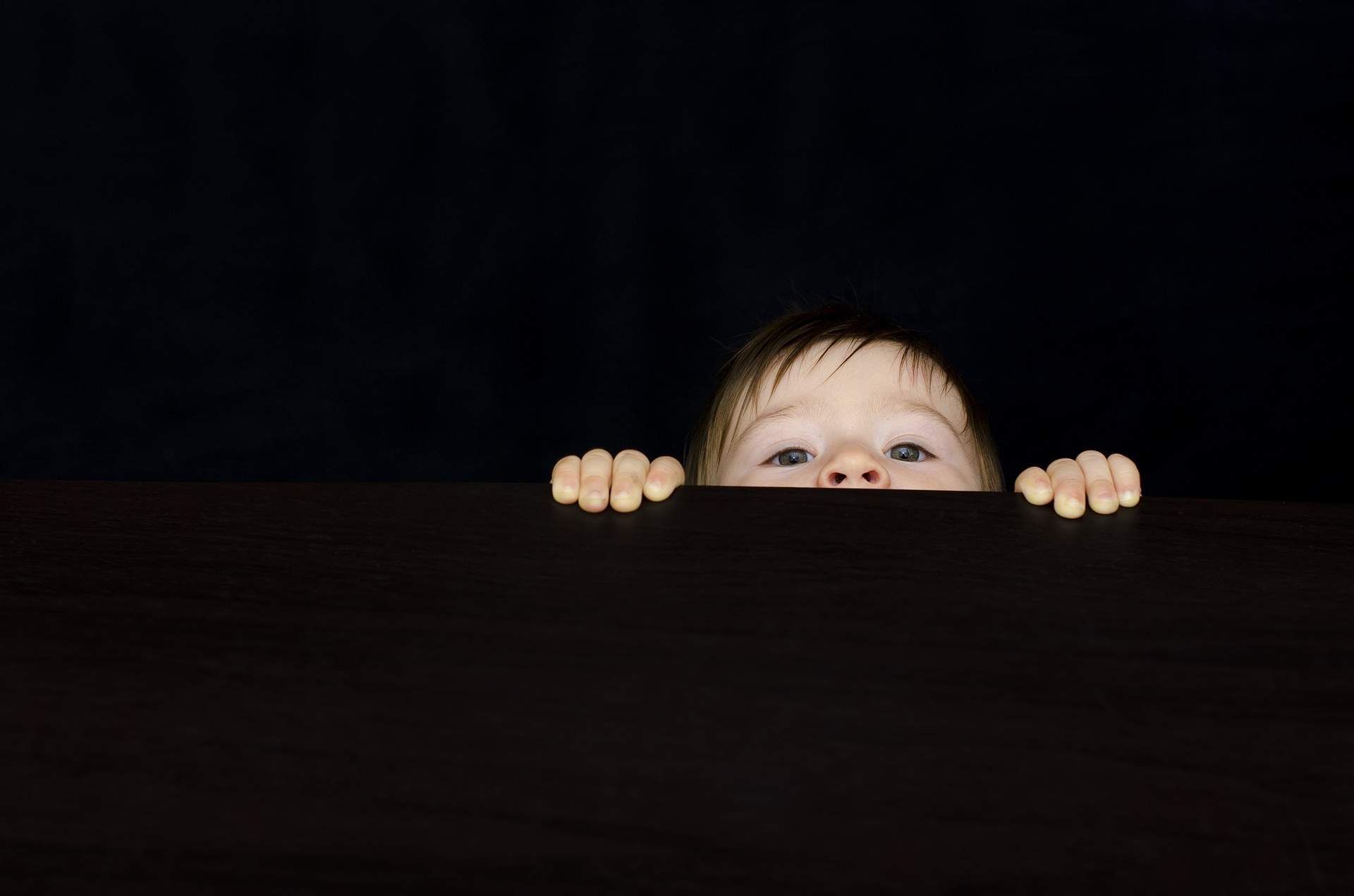 Black background with young child peeking over a ledge